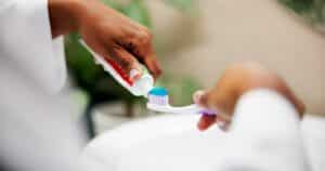 A photo of an individual putting toothpaste on a toothbrush right before they begin to brush their teeth